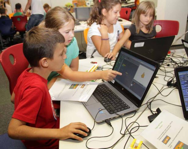 Eine Gruppe Kinder arbeitet an Laptops mit einer Programmieroberfläche.
