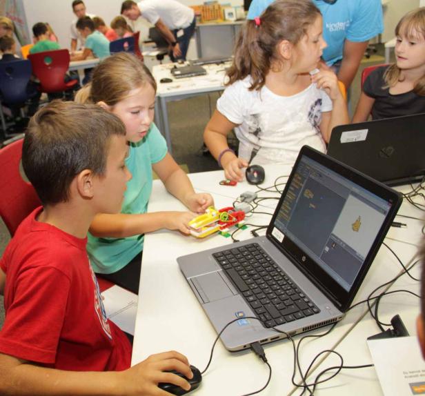 Kinder arbeiten an Laptops mit Robotik-Bausätzen in einem Klassenzimmer.