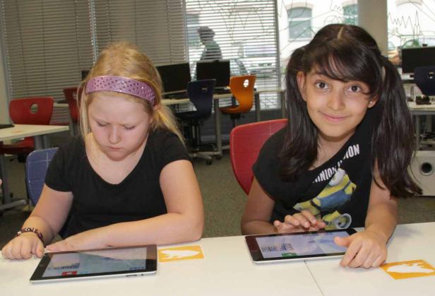 Zwei Mädchen sitzen an einem Tisch und benutzen Tablets.