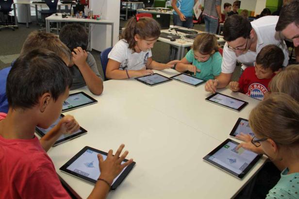 Eine Gruppe Kinder sitzt an einem Tisch und benutzt Tablets.