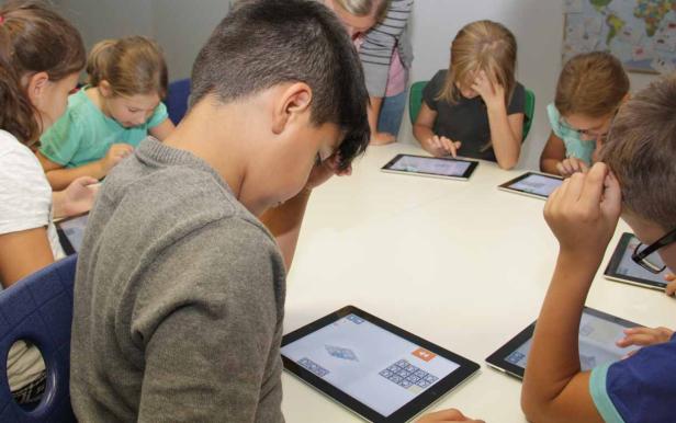 Eine Gruppe von Kindern sitzt an einem Tisch und benutzt Tablets.