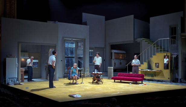 Szene aus einem Theaterstück mit mehreren Schauspielern auf einer gelben Bühne.