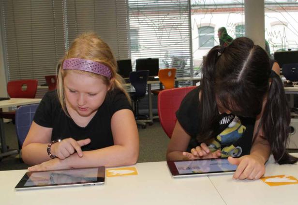 Zwei Mädchen sitzen an einem Tisch und benutzen Tablets.