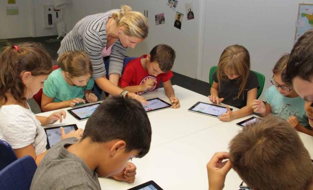 Eine Lehrerin hilft einer Gruppe von Kindern, die an einem Tisch mit Tablets arbeiten.