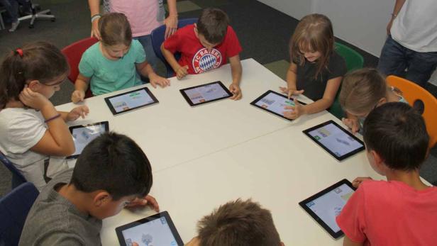 Kinder sitzen an einem Tisch und benutzen Tablets.