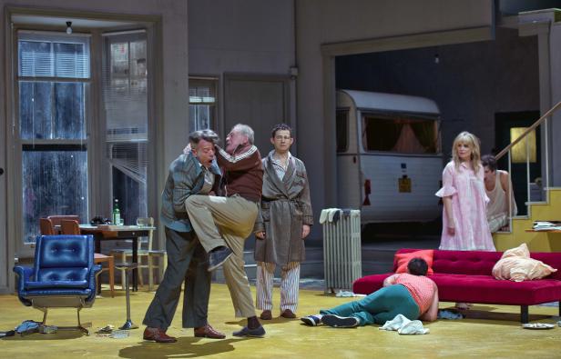 Auf einer Theaterbühne raufen sich zwei Männer, während andere Personen zusehen.