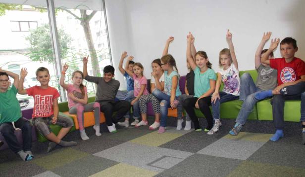 Eine Gruppe von Kindern sitzt auf einer Bank und hebt die Hände.