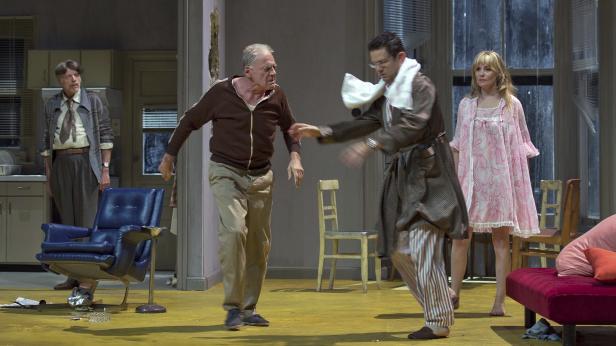 Vier Personen stehen in einem Wohnzimmer, möglicherweise während einer Theatervorstellung.
