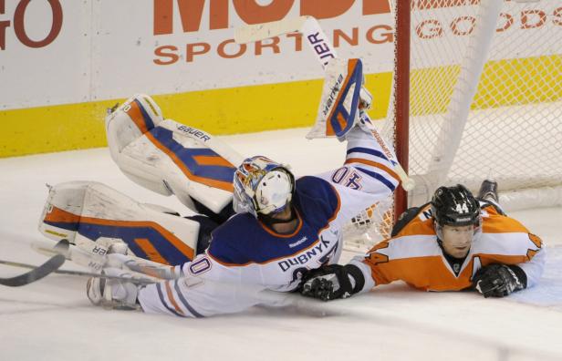 Ein Eishockeytorwart wehrt einen Schuss ab, während ein anderer Spieler auf dem Eis liegt.