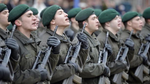 Eine Reihe von Soldaten in Uniform und grünen Baretts steht mit Gewehren stramm.