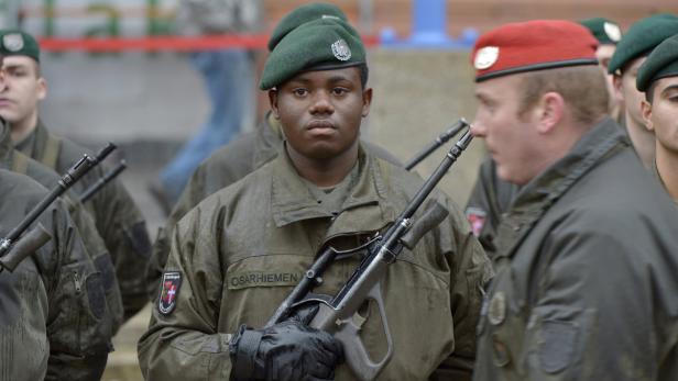 Soldaten in Uniformen und Baretts stehen mit Gewehren in einer Reihe.