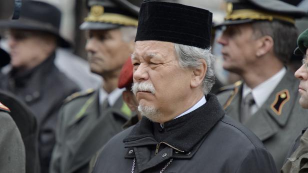 Ein Mann mit Bart und traditioneller Kopfbedeckung steht inmitten einer Gruppe von Militärangehörigen.