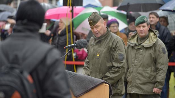 Ein Mann in Uniform spricht bei Regen vor einer Menschenmenge.
