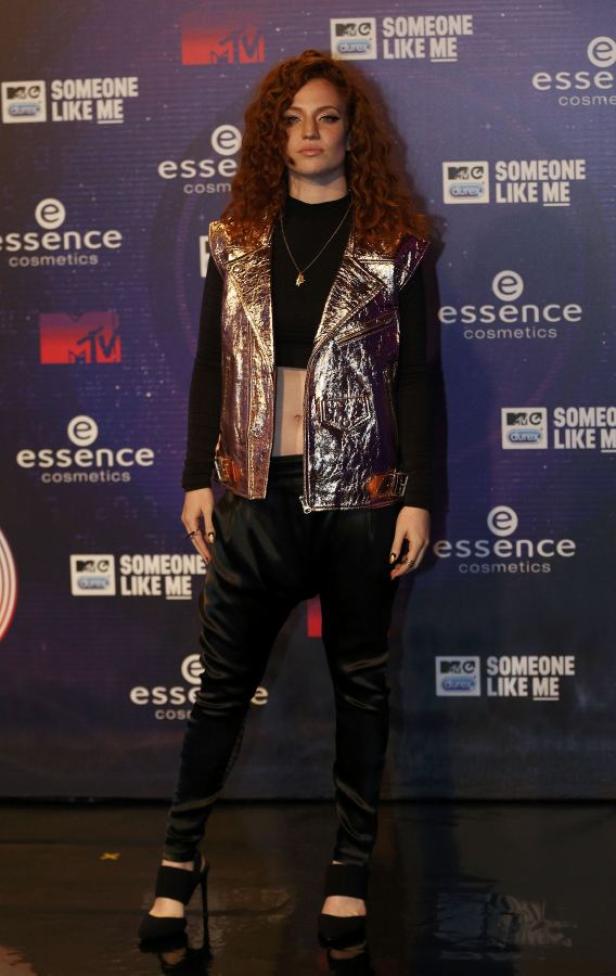 Eine Frau mit lockigem, rotem Haar posiert vor einer Wand mit Logos.