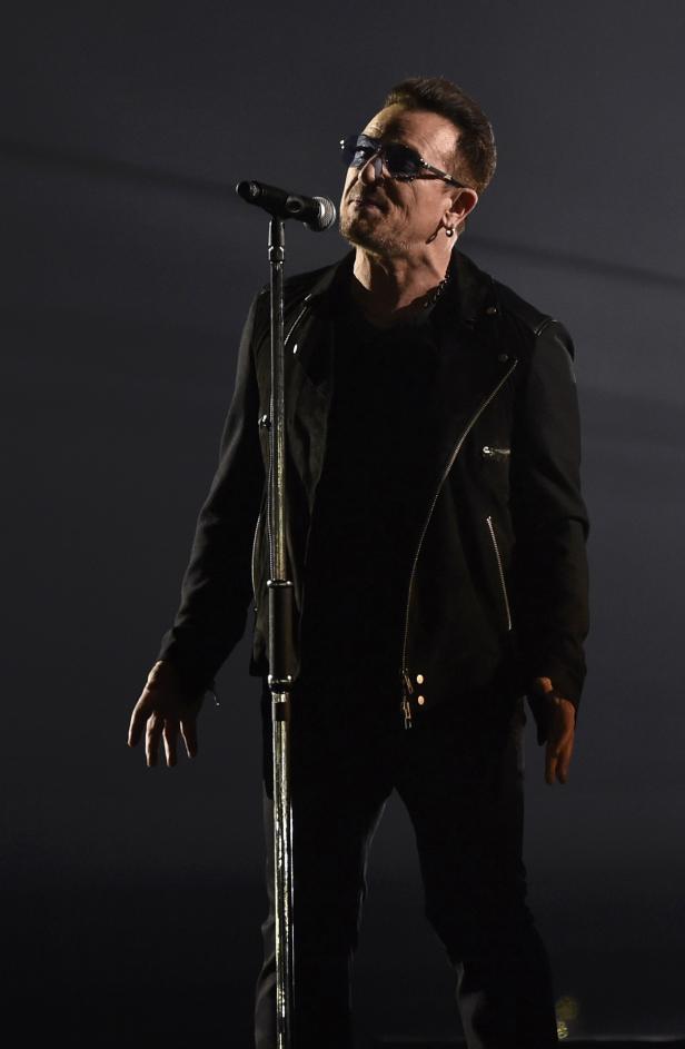 Bono von U2 singt in dunkler Kleidung vor einem Mikrofon.