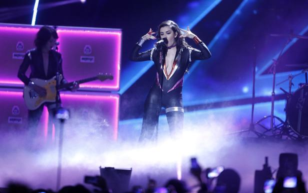Charli XCX tritt in einem schwarzen Glitzeranzug auf einer Bühne auf.