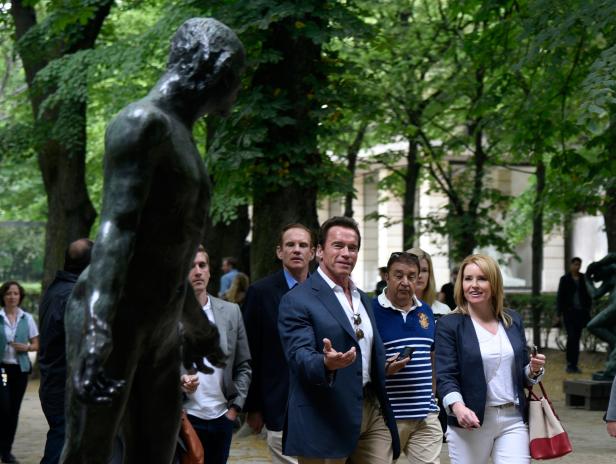 Arnold Schwarzenegger und eine Gruppe von Menschen besuchen einen Skulpturengarten.