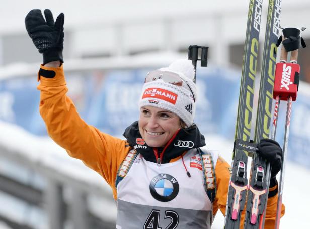 Eine Biathletin mit Skiern feiert mit erhobenem Arm.