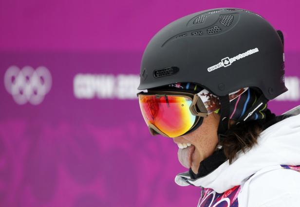 Eine Snowboarderin mit Helm und Brille streckt die Zunge heraus.