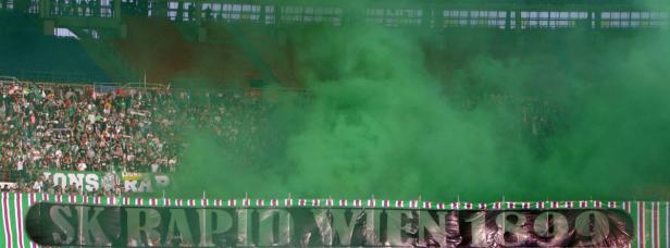 Grüne Rauchwolke vor einer Tribüne mit Fans des SK Rapid Wien.