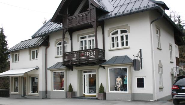 Ein zweistöckiges, weißes Gebäude mit einem dunklen Walmdach und einem Balkon.