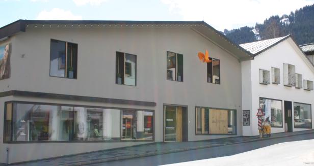 Ein zweistöckiges Gebäude mit Schaufenstern und einem orangefarbenen Dekorationselement am Fenster.