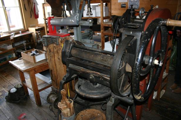 Eine alte Buchdruckmaschine steht in einer Werkstatt.