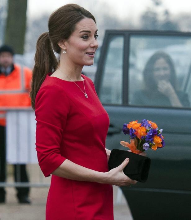 Kate Middleton in einem roten Kleid mit einem Blumenstrauß und einer Clutch in der Hand.