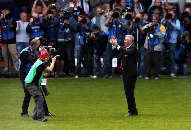 Alex Ferguson wird von einer Gruppe Fotografen auf einem Rasenplatz fotografiert.