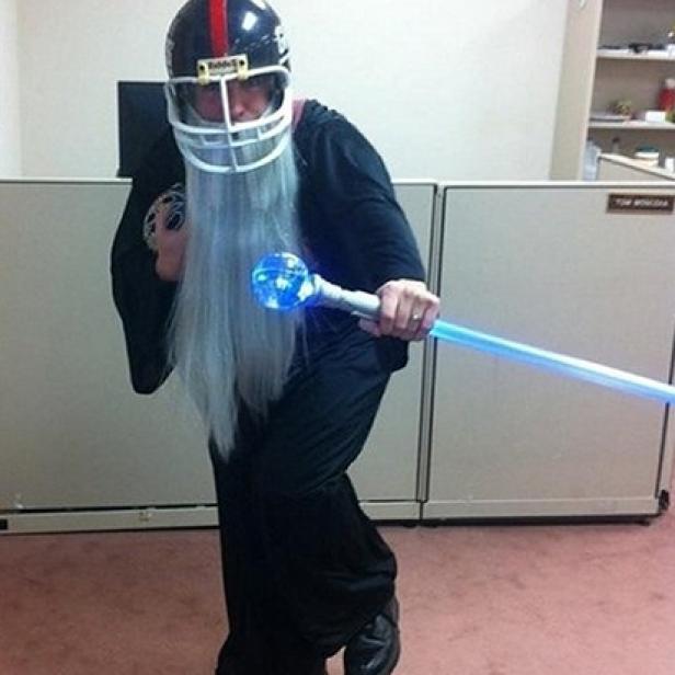 Eine Person in einem Zaubererkostüm mit Footballhelm und leuchtendem Stab.