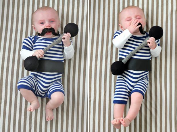Zwei Babys in gestreiften Badeanzügen posieren mit Spielzeug-Hanteln und Schnurrbärten.