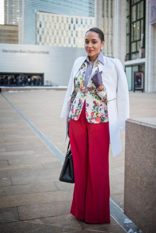 Eine Frau mit roter Hose und Blumenjacke posiert vor einem Gebäude.