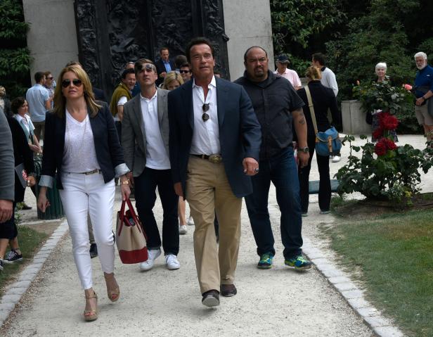 Arnold Schwarzenegger geht mit einer Gruppe von Menschen auf einem Kiesweg entlang.