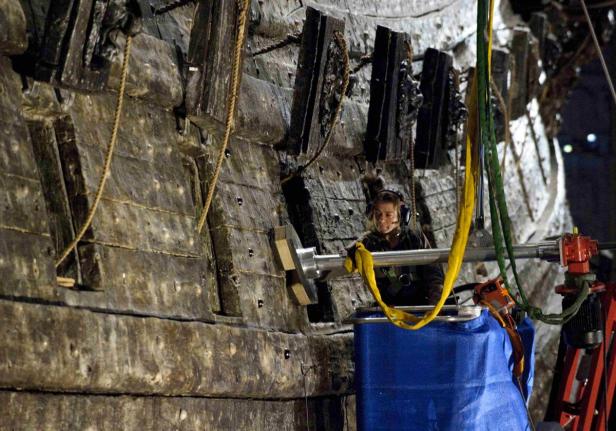 Eine Frau arbeitet an der Restaurierung eines alten Holzschiffs.