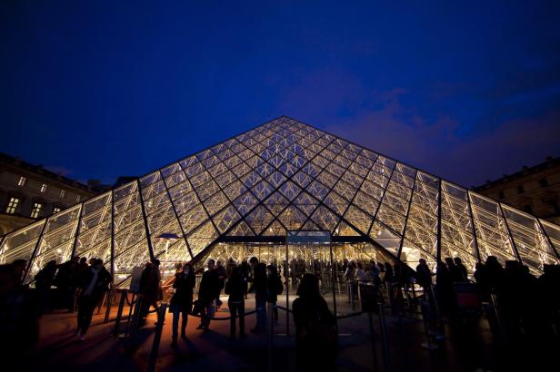Die Glaspyramide des Louvre-Museums in Paris bei Nacht mit Menschen davor.