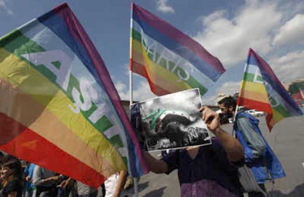 Menschen demonstrieren mit Regenbogenfahnen und einem Foto.