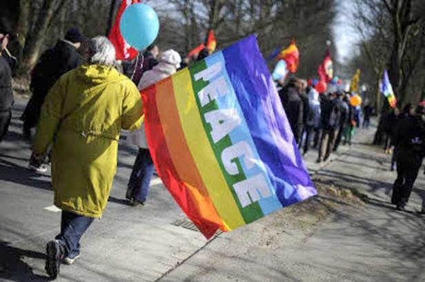 Menschen demonstrieren mit einer Regenbogenflagge mit der Aufschrift „Peace“.