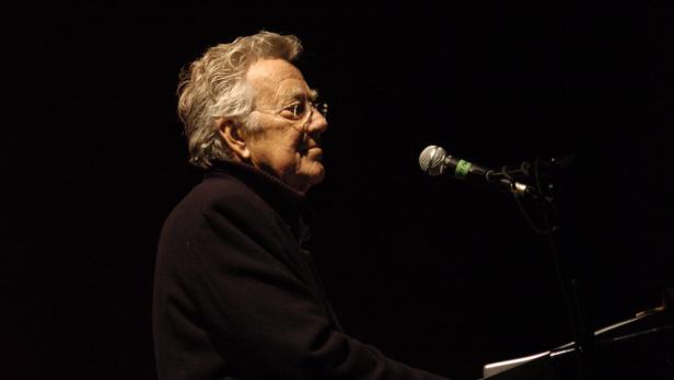 Ein älterer Mann mit Brille singt in ein Mikrofon.