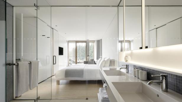 Blick durch eine Glastür auf ein modernes Schlafzimmer mit Doppelwaschbecken im Vordergrund.