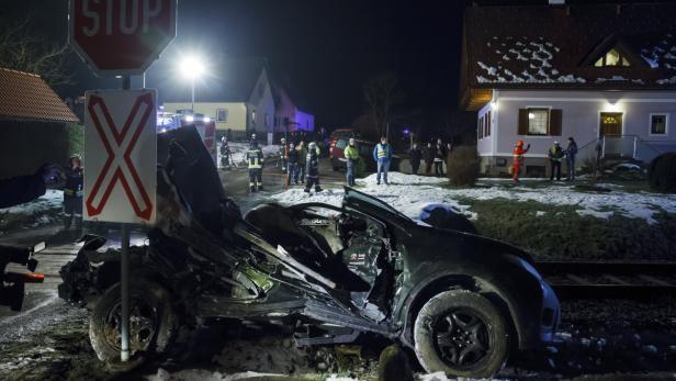 STEIERMARK: ZUGUNFALL MIT PKW - VIER TOTE Ein schwer beschädigtes Auto steht an einem Bahnübergang, umgeben von Rettungskräften.