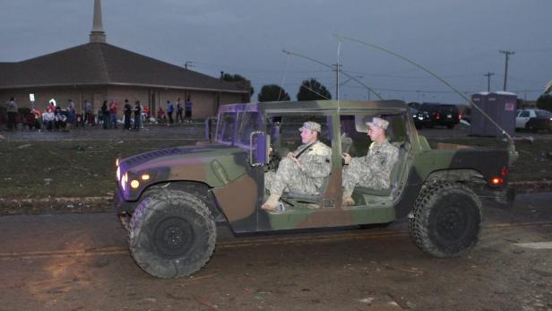 Zwei Soldaten fahren in einem Militärfahrzeug durch ein zerstörtes Gebiet.