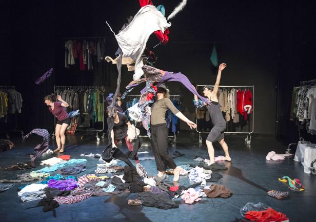Mehrere Tänzer interagieren mit Kleidung auf einer Bühne.