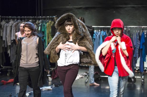 Drei Frauen posieren in unterschiedlicher Kleidung vor einem Kleiderständer.