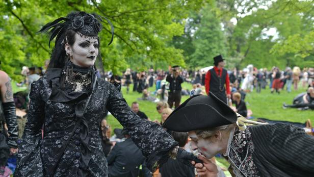 Ein Mann im Kostüm küsst die Hand einer Frau im viktorianisch-inspirierten Gothic-Outfit auf einer Wiese.
