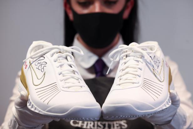 A Christie's gallery assistant poses with sneakers from the 'The Championships, Wimbledon, 2007' lot included in 'The Roger Federer Collection', due to be sold at auction, at Christie's auction house in London