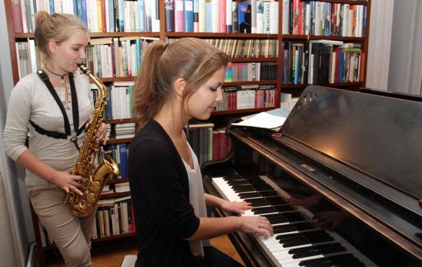 Eine junge Frau spielt Klavier, während eine andere Saxophon spielt.