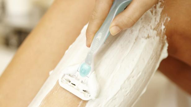 Eine Frau rasiert ihr mit Rasierschaum bedecktes Bein mit einem Rasierer.