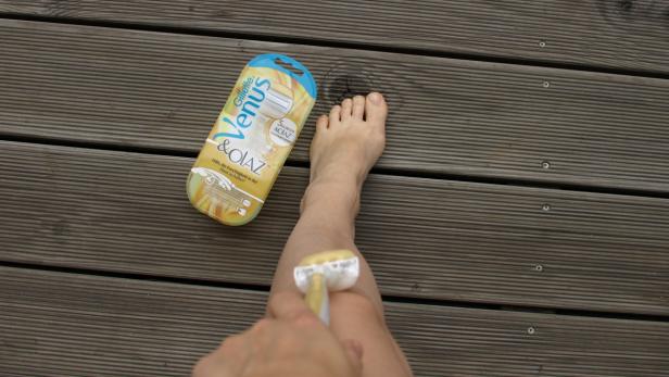 Eine Frau rasiert sich das Bein mit einem Gillette Venus Rasierer auf einer Holzterrasse.