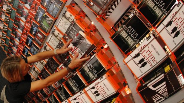Eine Frau greift in einem Buchladen nach einem Buch in einem Regal voller Thriller.