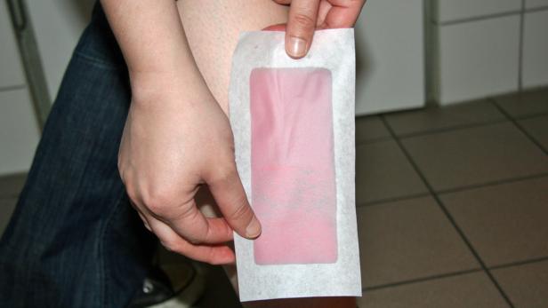 Eine Person entfernt Haare mit einem Wachsstreifen vom Bein.